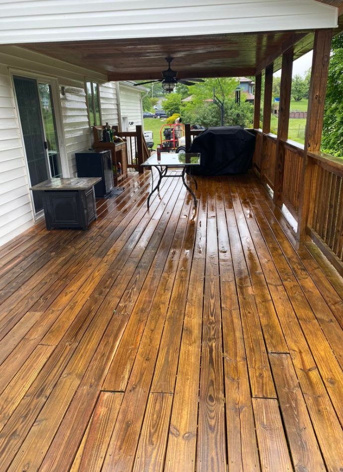 A freshly stained wooden deck with a ceiling fan, grill, and outdoor furniture. The warm brown tones of the wood create an inviting outdoor home space.